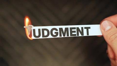 Hand holding a paper label reading JUDGMENT as the edge burns in flame Stock Footage 333652949