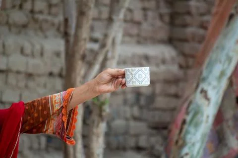 Hand holding a patterned tea cup in a rustic outdoor village setting Stock-Fotos