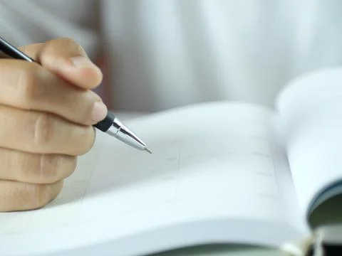 Hand holding pen writing on note paper. Finance business concept. Copy space. Stock Photos