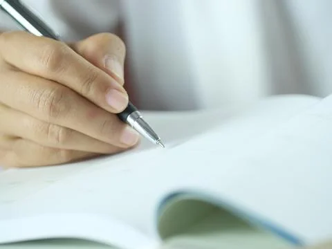 Hand holding pen writing on note paper. Finance business concept. Copy space. Stock Photos