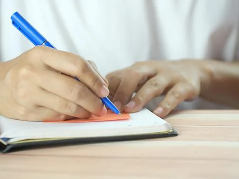 Hand holding pen writing on note paper. Finance business concept. Copy space. Stock Photos
