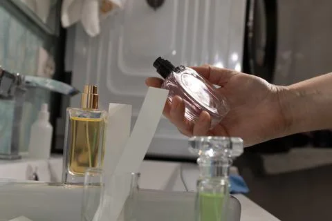Hand holding perfume bottle angled toward palm on bathroom vanity Stock Photos