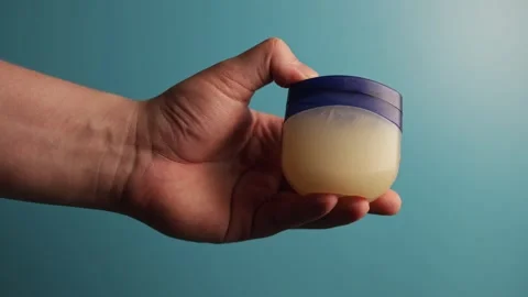Hand holding petroleum jelly jar against a blue background Stock Footage 340268410