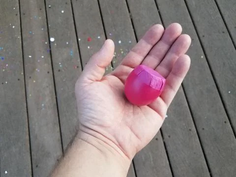 Hand holding pink egg shell with confetti on wood deck Stock Photos