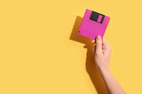 Hand holding a pink floppy disk on a yellow background, retro technology and  Stock Photos
