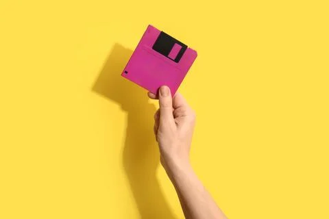 Hand holding pink floppy disk on yellow background, retro technology and data Stock Photos