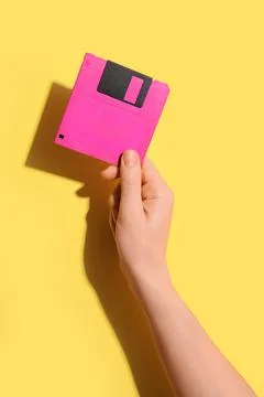 Hand holding pink floppy disk on yellow background, retro technology and data Stock Photos
