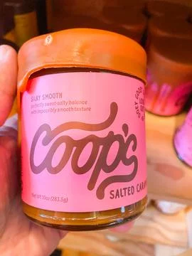 A hand holding a pink jar of Coop's Salted Caramel sauce with a dripping ca.. Stock-Fotos