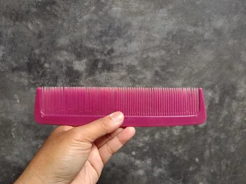 Hand Holding a Pink Plastic Comb Against a Textured Background. Stock Photos