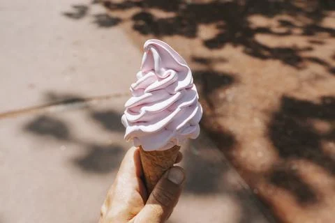 Hand holding a pink soft-serve ice cream cone in a park. 写真素材