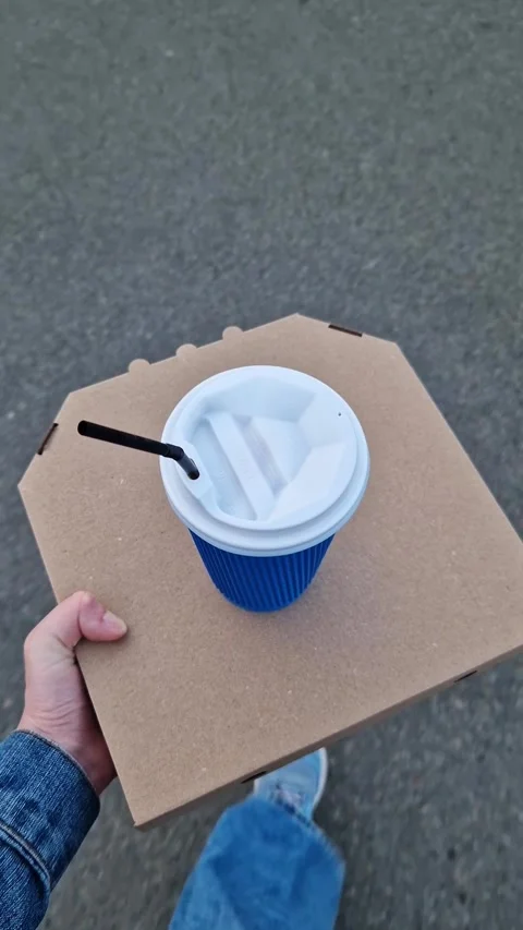 Hand holding pizza box and paper coffee cup on asphalt background Stock Footage 335198480