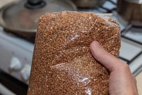 Hand holding a plastic bag of raw buckwheat grains in the kitchen Stock Photos