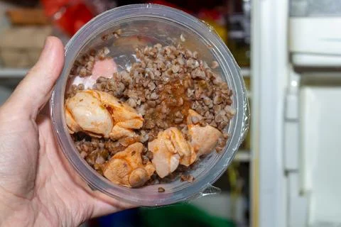 Hand holding plastic container with cooked buckwheat and marinated raw Stock Photos
