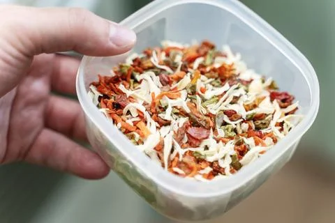 Hand holding a plastic container filled with dried vegetables for seasoning Stock Photos