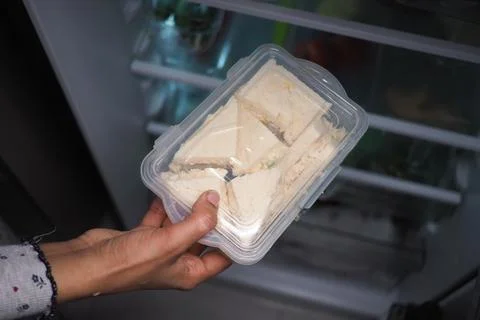 Hand Holding Plastic Container of Triangular White Bread Sandwiches Pulled From Stock Photos