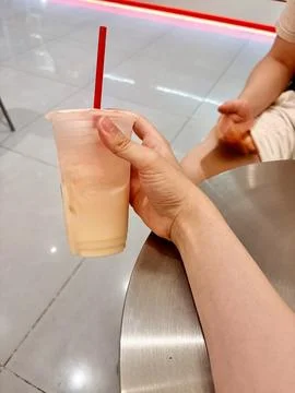 Hand holding a plastic cup with a red straw on a metal table. Stock Photos