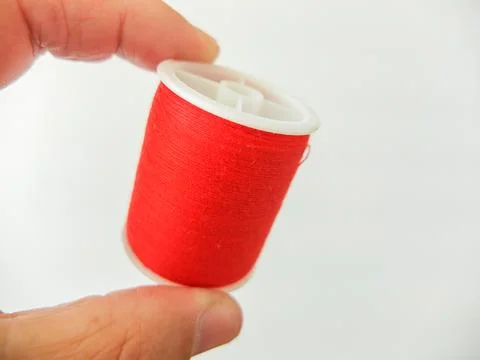 Hand holding a plastic spool of bright red sewing thread isolated on white. Foto stock