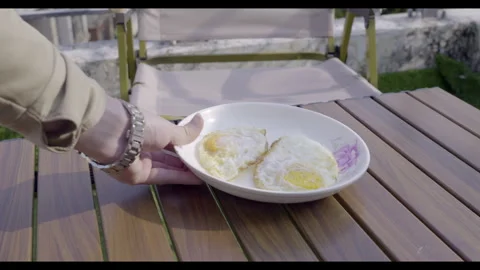 Hand Holding Plate with Two Fried Eggs on Wooden Table in Morning Sunlight – 4K  Stock Footage 327055103