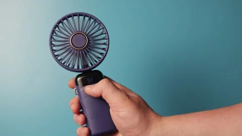 Hand holding a portable fan with digital display against a blue background Stock Footage 340265576