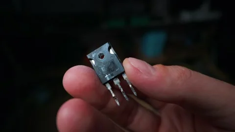 Hand Holding a Power Transistor Electronic Component Against Dark Background Stock Footage 339364355