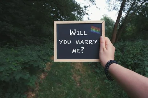 Hand Holding Proposal Sign with Rainbow Flag in Forest Setting Stock Photos