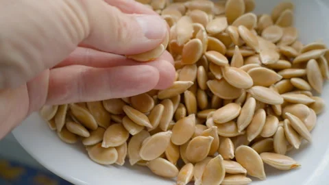 Hand Holding Pumpkin Seed Over Bowl Full of Seeds Stock Footage 318724678