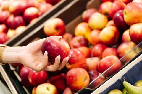 Hand holding red apple while choosing fresh fruit at market display with wooden Stock Photos