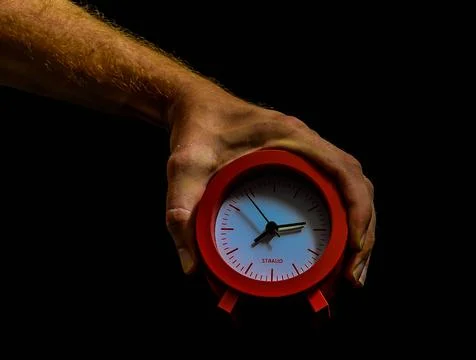 A hand holding a red clock with the hands at the numbers 3 and 9 Foto stock