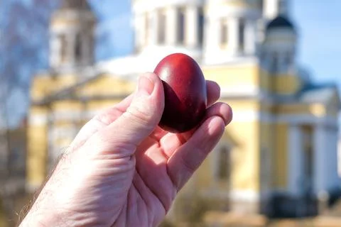 Hand holding red dyed Easter egg against blurred Orthodox church background.. Stock Photos