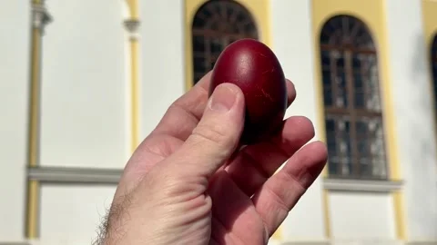 Hand holding a red Easter egg in front of an Orthodox church Video stock 332736099