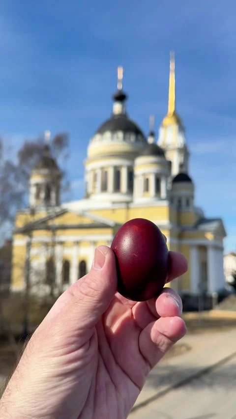 Hand holding a red Easter egg in front of an Orthodox church Video stock 332736343