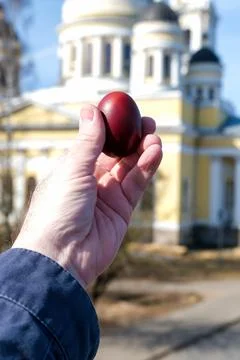 Hand holding a red Easter egg in front of a church, symbolizing preparation f Stockfoto's