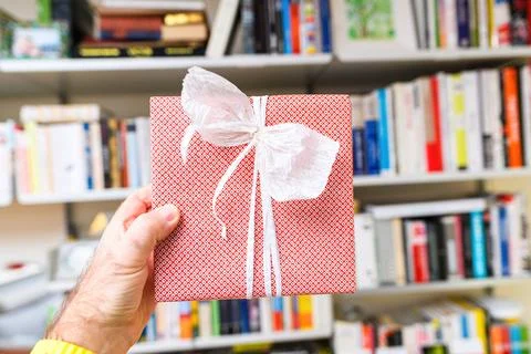 Hand Holding Red Gift in Front of Bookshelf Stock Photos