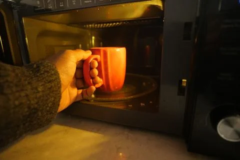 Hand holding red mug while using microwave at home Stock Photos