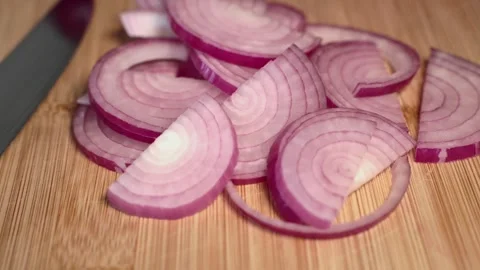 A hand is holding a red onion on a cutting board and slicing it with a knife. Stock Footage 341345802