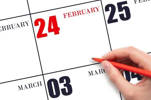 A hand holding a red pen and pointing on the calendar date February 24. Red c Stock Photos