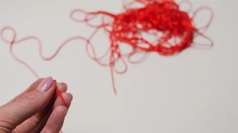 Hand holding red thread with tangled yarn in the background Stock Photos