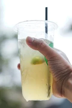 Hand holding a refreshing cold lime drink in a plastic cup with a straw, pe.. 库存照片
