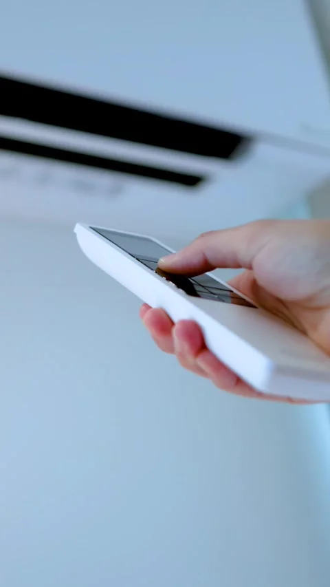 Hand Holding Remote Control to Adjust Wall Mounted Air Conditioner Stock Footage 337917840