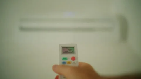 Hand holding a remote control, adjusting temperature and fan settings for an Stock Footage 343266589