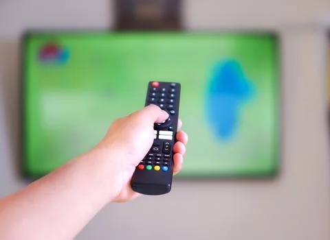A hand holding a remote control aimed at a television Stock Photos