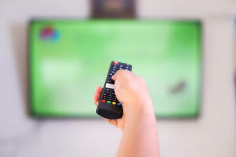 A hand holding a remote control aimed at a television Stock Photos
