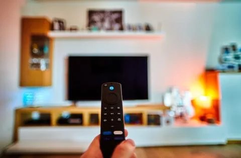 Hand holding a remote control in a blurred living-room Stock Photos