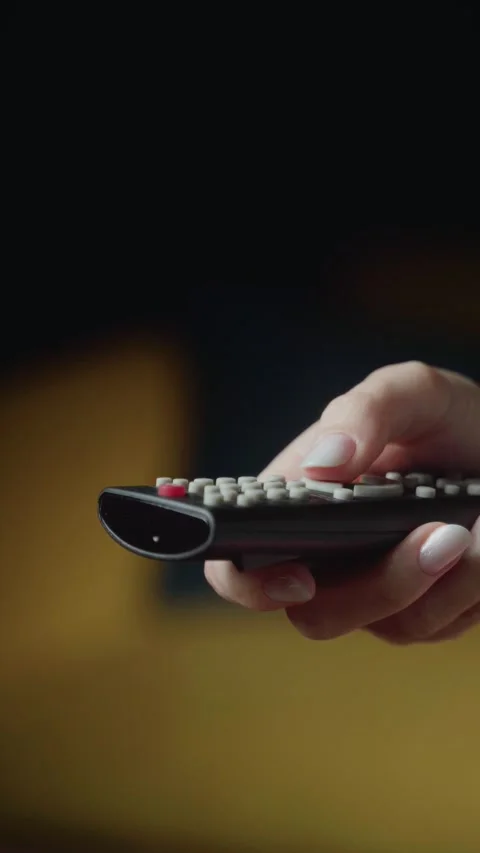 Hand holding a remote control in a cozy living room setting during a quiet Stock-Footage 303768659