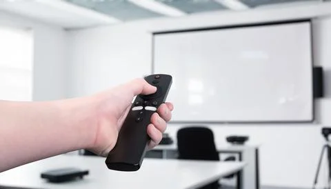 Hand holding a remote control, operating a projector in a conference room Foto stock