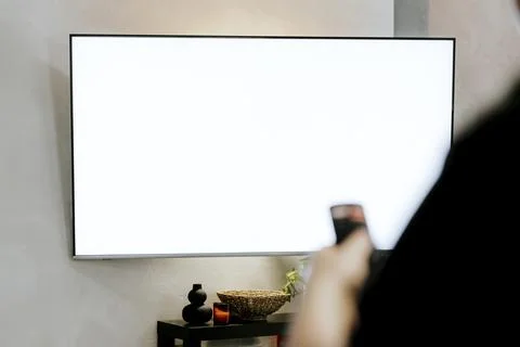 Hand holding remote control pointing to TV. Person watching smart television. Stock Photos