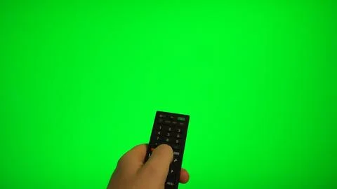 Hand holding remote control pointing at green screen TV mockup. Stock Photos