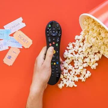 Hand holding remote control popcorn movie tickets Фото