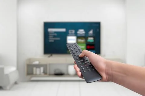 Hand holding a remote control for a smart TV, featuring app buttons Stock Photos