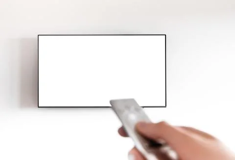 Hand holding remote control to switch channels on wall television. Modern s.. 库存照片